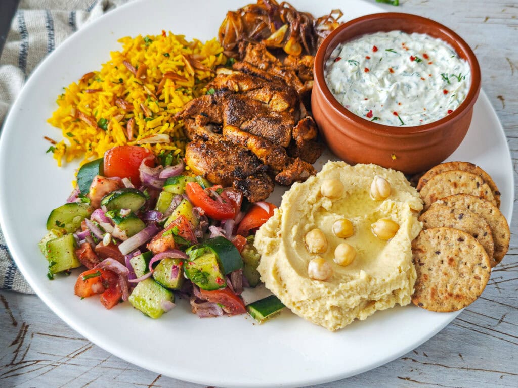 Mediterranean Chicken Shawarma Plate Chicken shawarma rice bowl containing shawarma chicken, Mediterranean yellow rice, Cucumber salad, hummus and tzatziki.