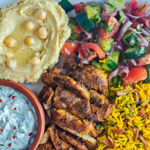 Mediterranean Chicken Shawarma Plate Chicken shawarma platter containing shawarma chicken, Mediterranean yellow rice, Cucumber salad, hummus and tzatziki.