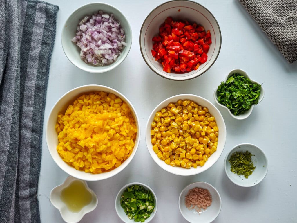Ingredients for spicy mango salsa recipe with corn in separate bowls.