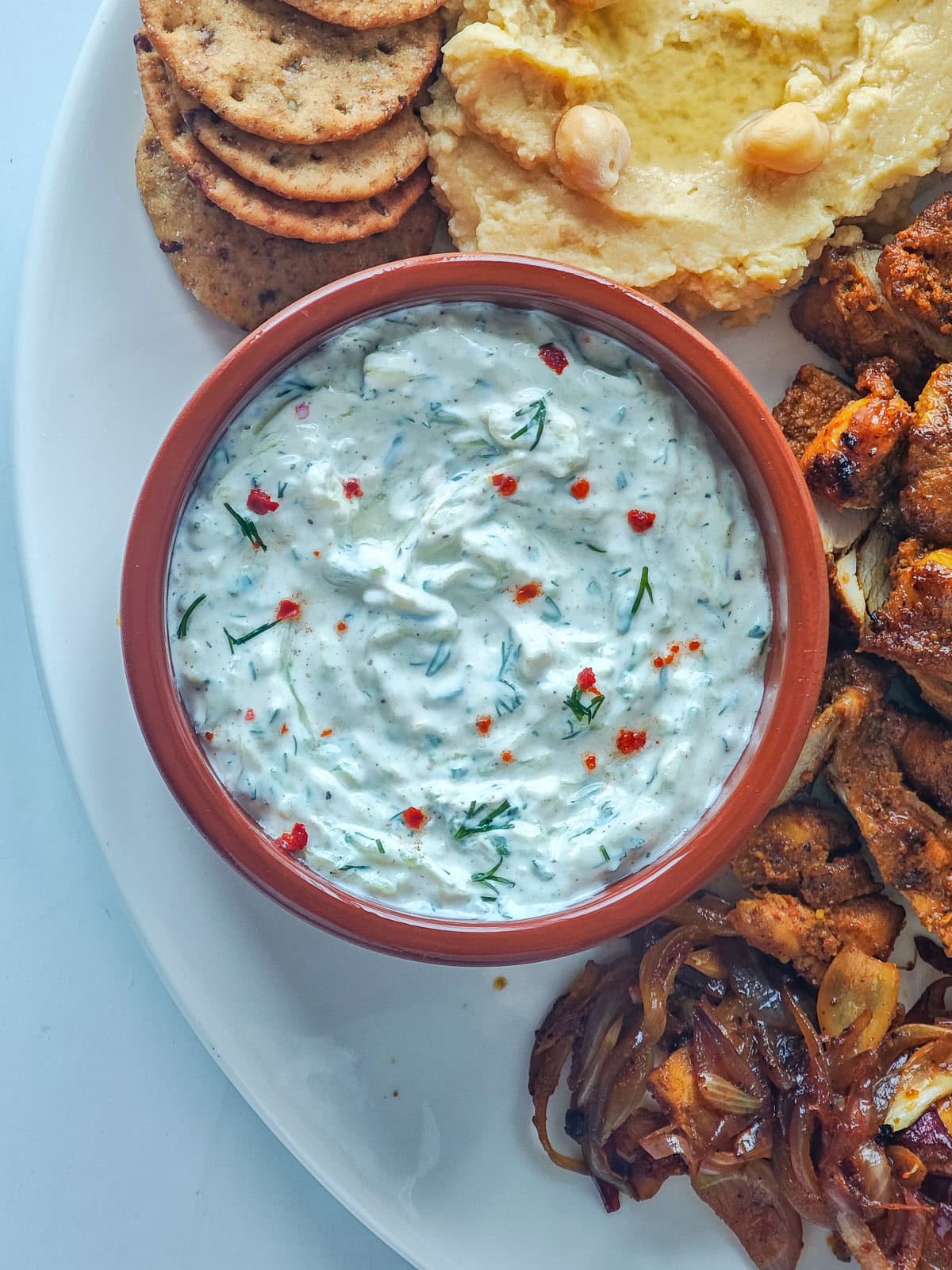 Creamy Cucumber Dill Tzatziki (Greek Yogurt Cucumber Dip) Creamy tzatziki in a brown bowl on a chicken shawarma plate.