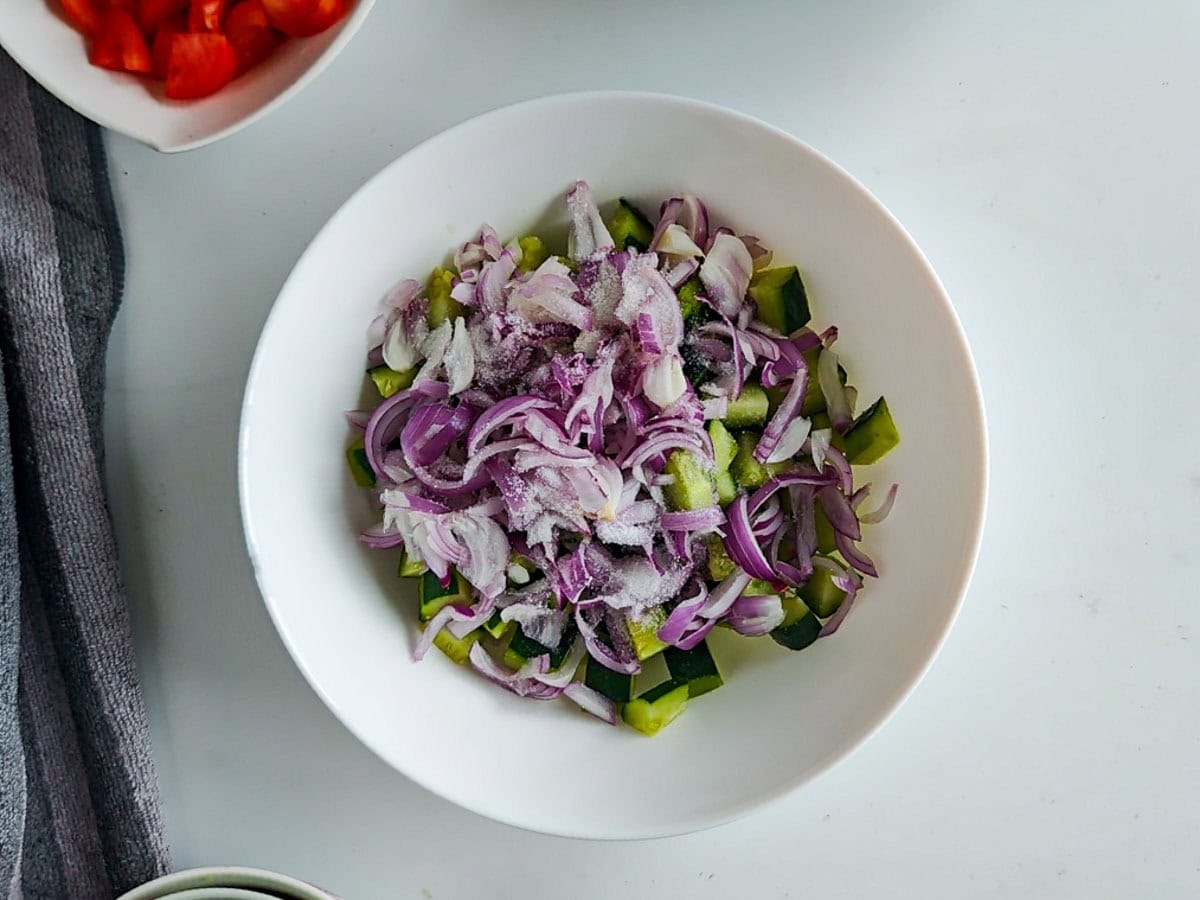 Quick Cucumber Tomato Mediterranean Salad (no dressing required) diced cucumbers and sliced onions with salt in a white bowl.