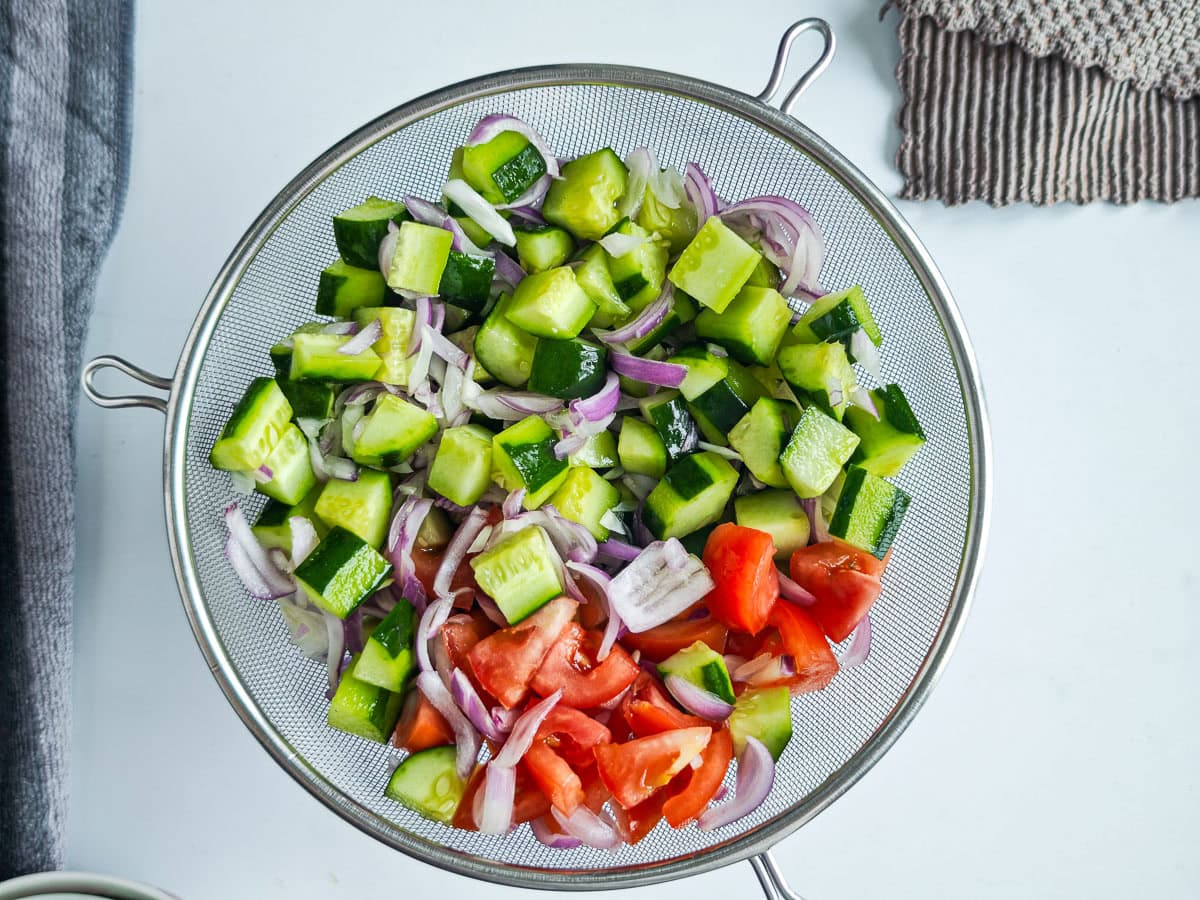 Quick Cucumber Tomato Mediterranean Salad (no dressing required) Cucumbers, onions and tomatoes in a colander.