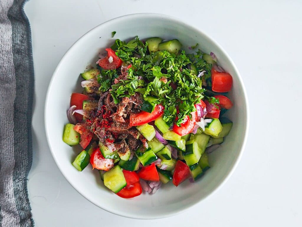 Vegetables and herbs for Mediterranean cucumber salad in a white bowl.