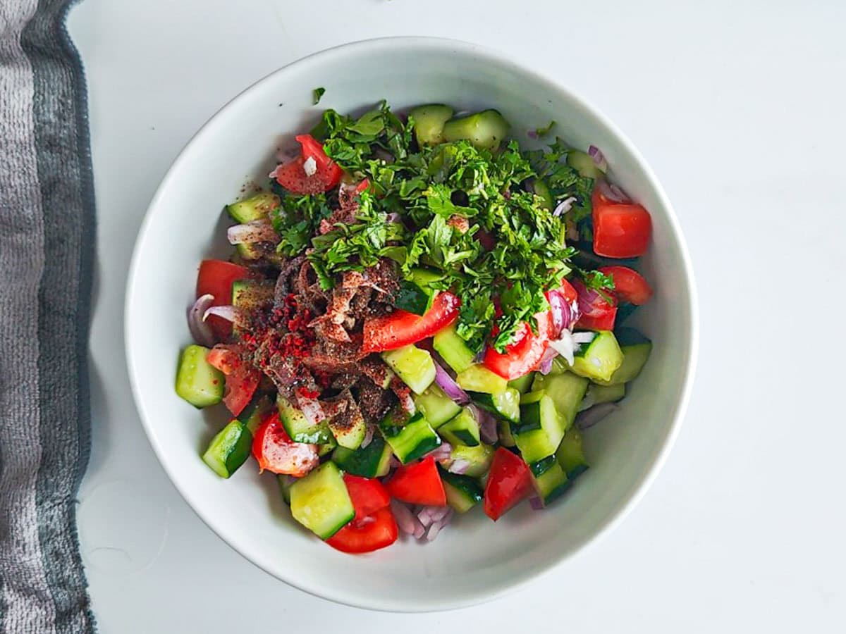 Quick Cucumber Tomato Mediterranean Salad (no dressing required) Vegetables and herbs for Mediterranean cucumber salad in a white bowl.