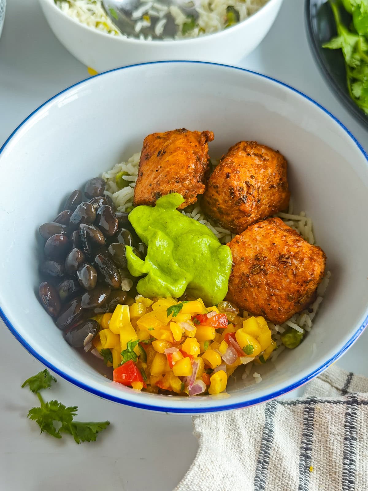 Easy Avocado Crema with Greek Yogurt Salmon taco bowl with avocado crema, lime cilantro rice, mango corn salsa and black beans in a white bowl.