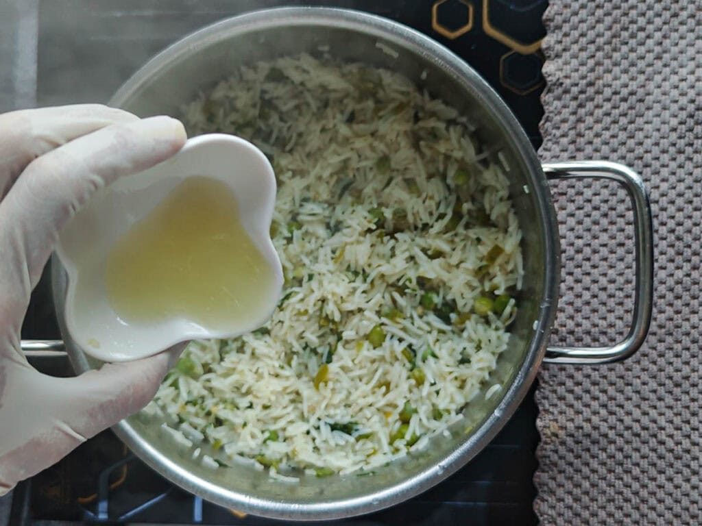 Lime juic being added from a small bowl to cooked basmati rice in a large pot.