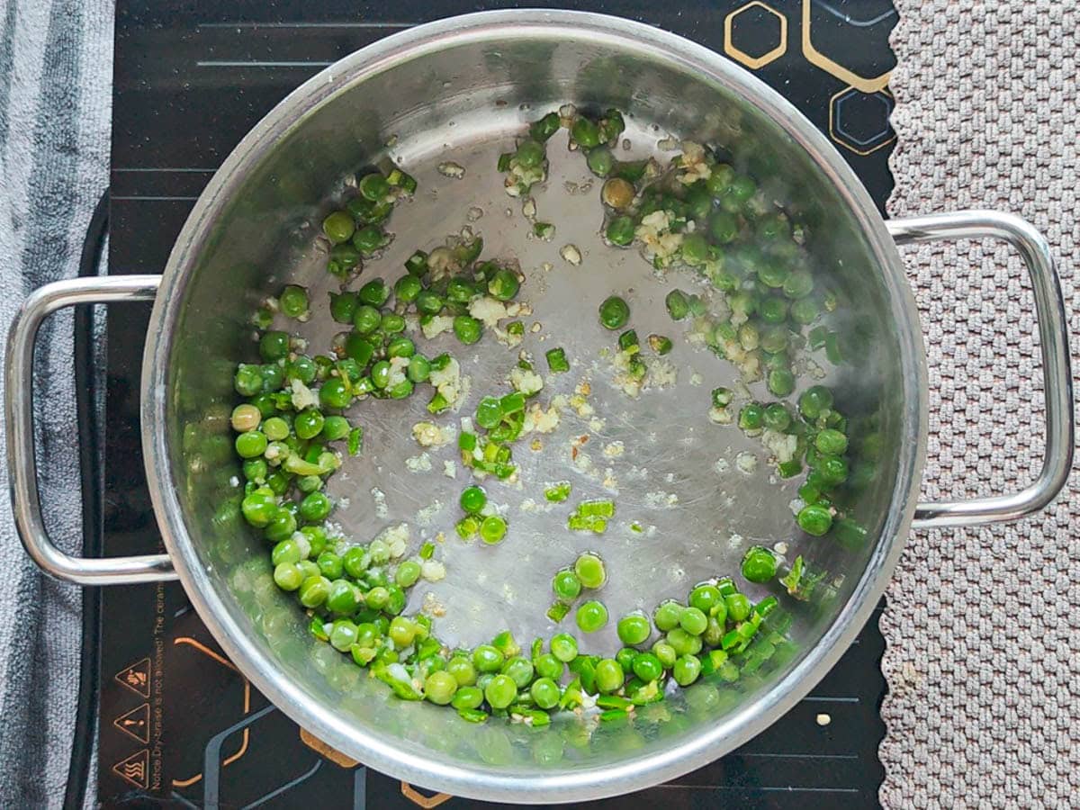 Easy One Pot Cilantro Lime Basmati Rice Minced garlic, jalapenos and green peas being sauteed in oil in a pot.