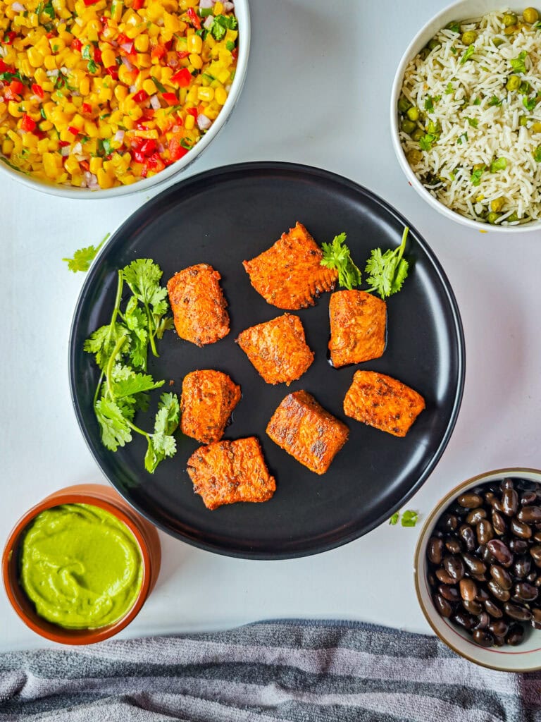 Components of Mexican salmon bowl: salmon, salsa, rice beans and avocado crema in separate bowls.