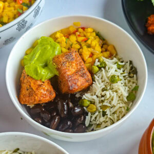 Healthy Salmon Taco Bowls with Avocado Crema Salmon taco bowl with taco-seasoned salmon, lime cilantro rice, mango corn salsa, black beans and avocado crema in a bowl.