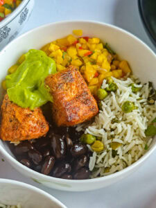 Salmon burrito bowl with taco-seasoned salmon, lime cilantro rice, mango corn salsa, black beans and avocado crema in a bowl.