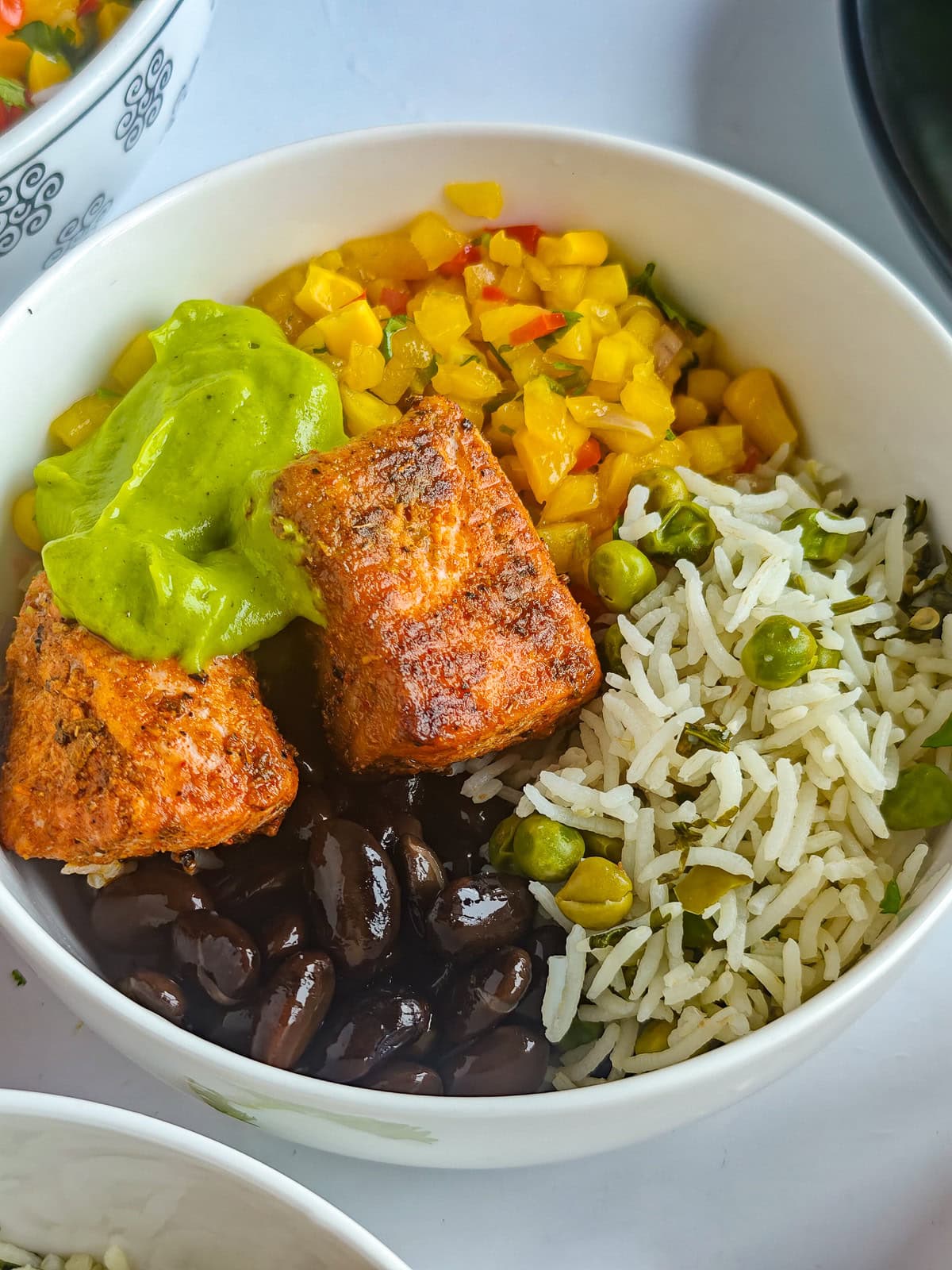 Healthy Salmon Taco Bowls with Avocado Crema Salmon burrito bowl with taco-seasoned salmon, lime cilantro rice, mango corn salsa, black beans and avocado crema in a bowl.