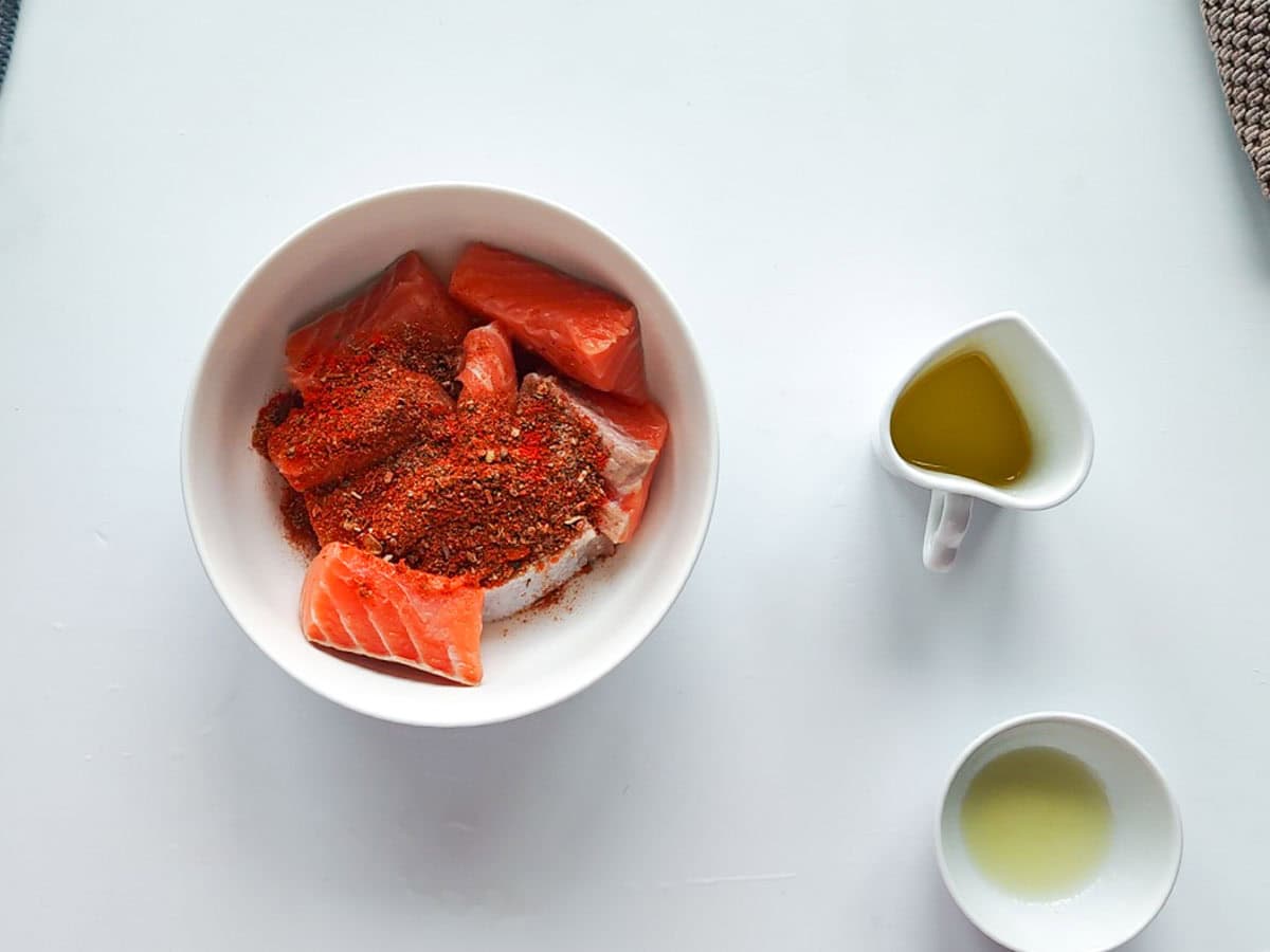 Healthy Salmon Taco Bowls with Avocado Crema Salmon with taco seasoning in a bowl with lemon juice and oil next to it.