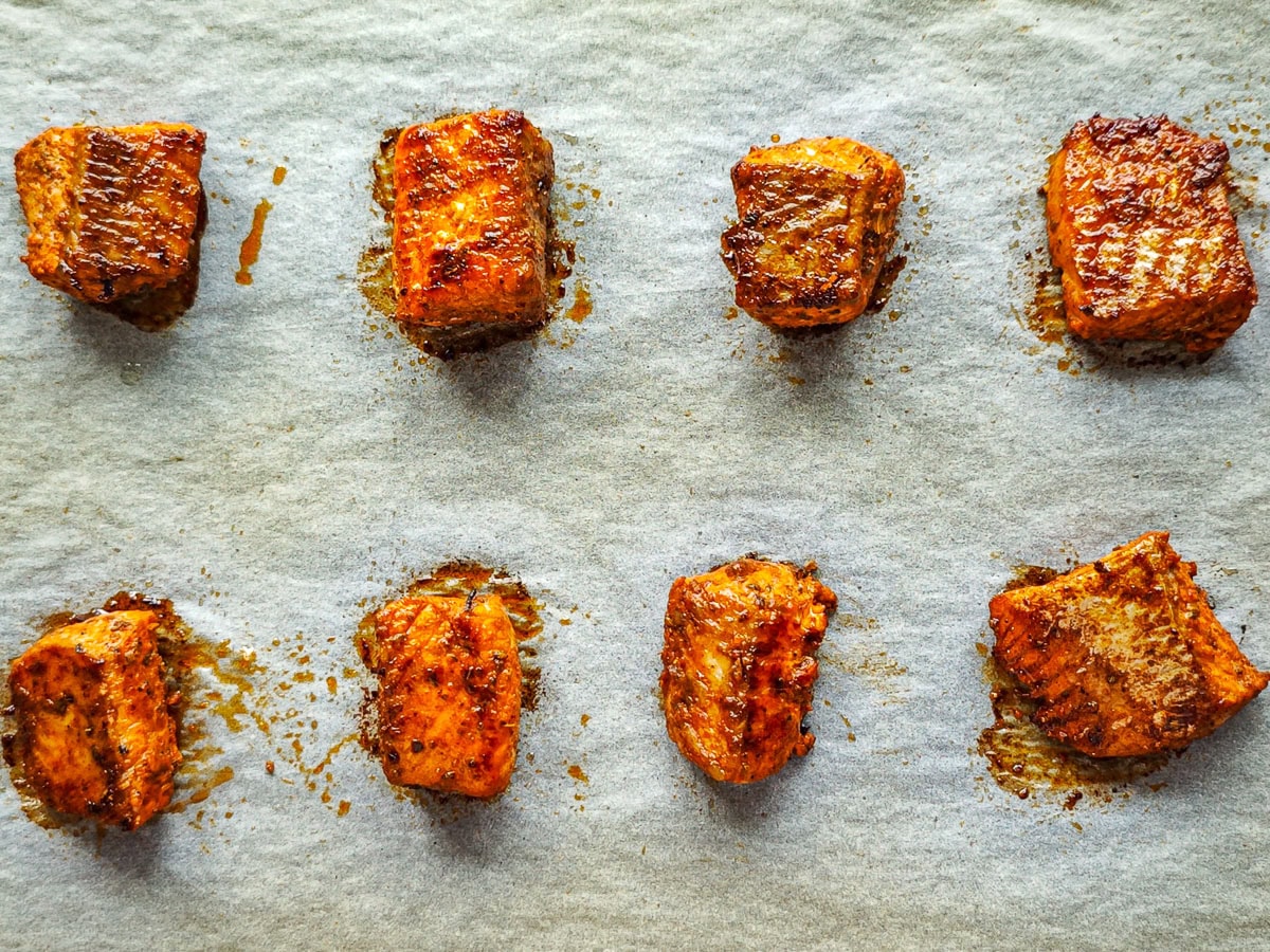 Healthy Salmon Taco Bowls with Avocado Crema Baked taco seasoned salmon cubes on a baking sheet.