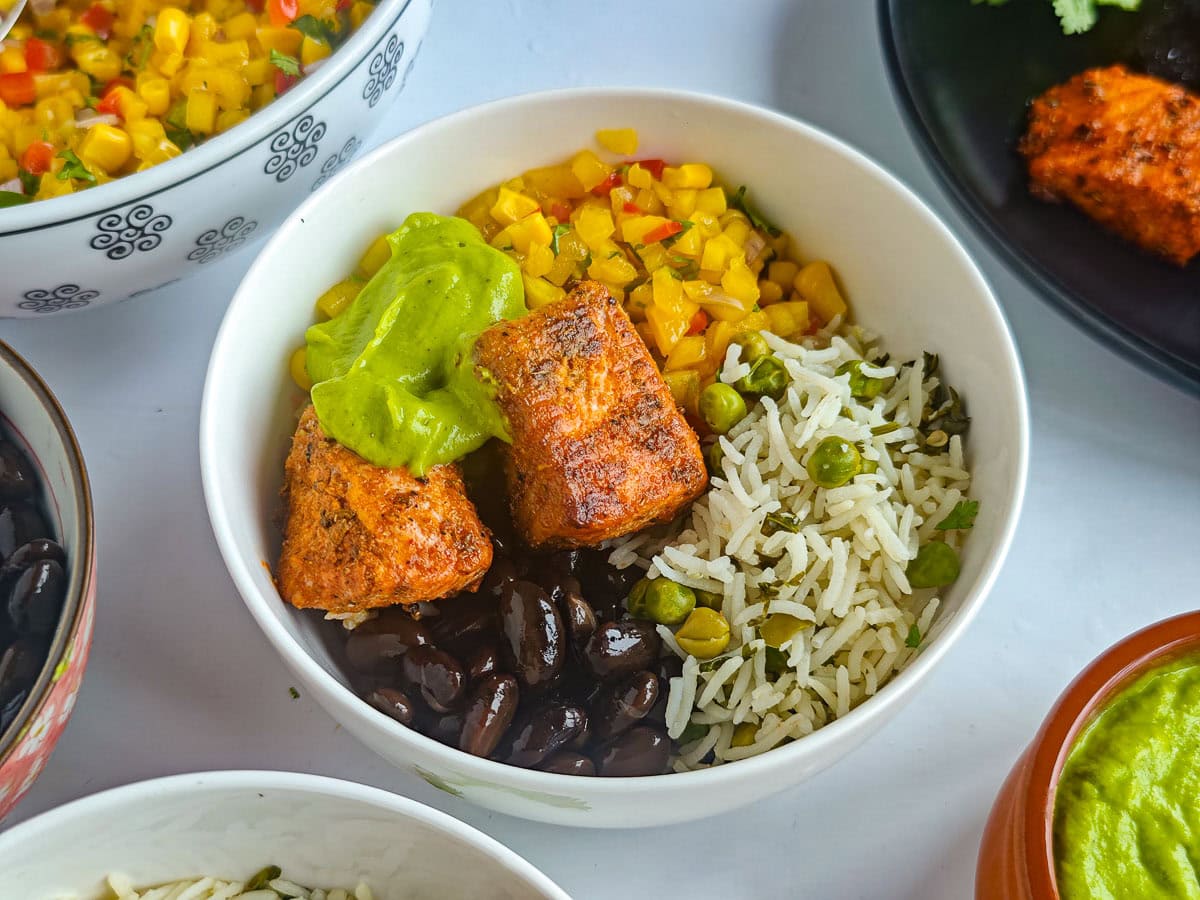 Healthy Salmon Taco Bowls with Avocado Crema Salmon burrito bowl with taco-seasoned salmon, lime cilantro rice, mango corn salsa, black beans and avocado crema in a bowl.