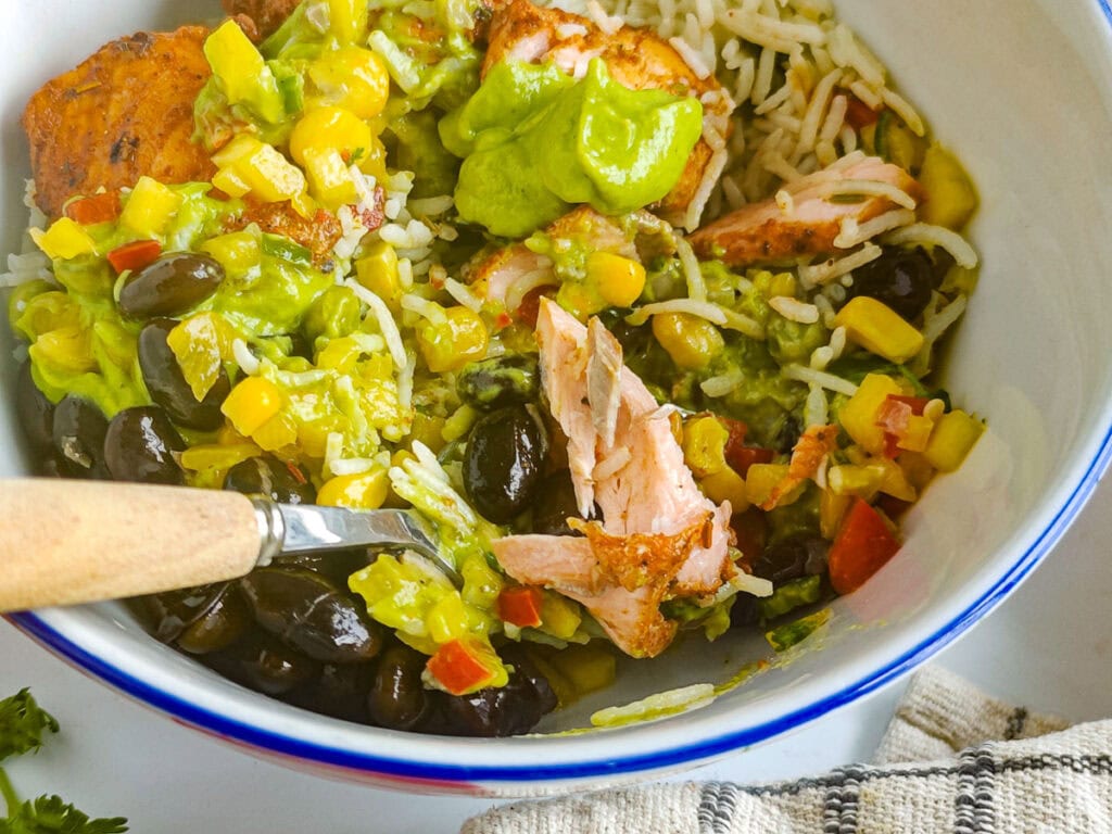 Salmon rice bowl with taco seasoned salmon, salsa, rice, beans and avocado crema.