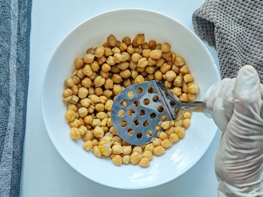 Chickpeas being mashed for salad in a bowl.