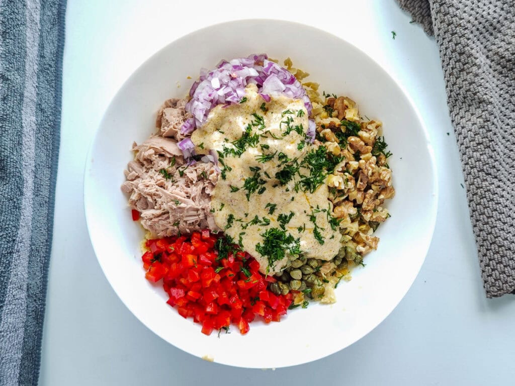 Flaked tuna, mashed chickpeas, bell peppers, onions and capers with yogurt dressing in a large white bowl.