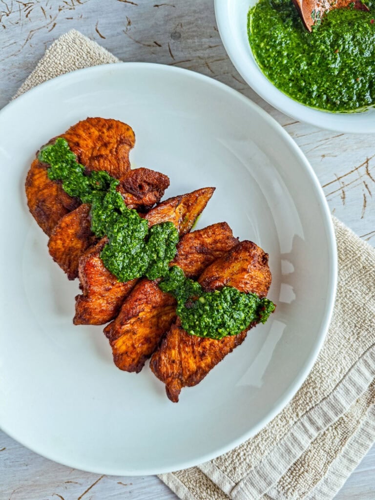 Chimichurri with basil drizzled on roasted chicken on a white plate.