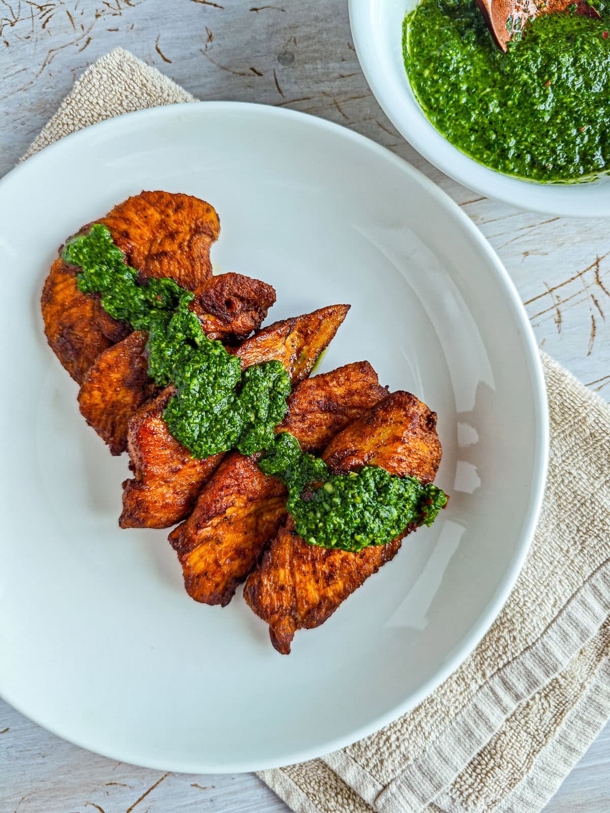 Low-calorie Basil Chimichurri (without excess oil) Chimichurri with basil drizzled on roasted chicken on a white plate.