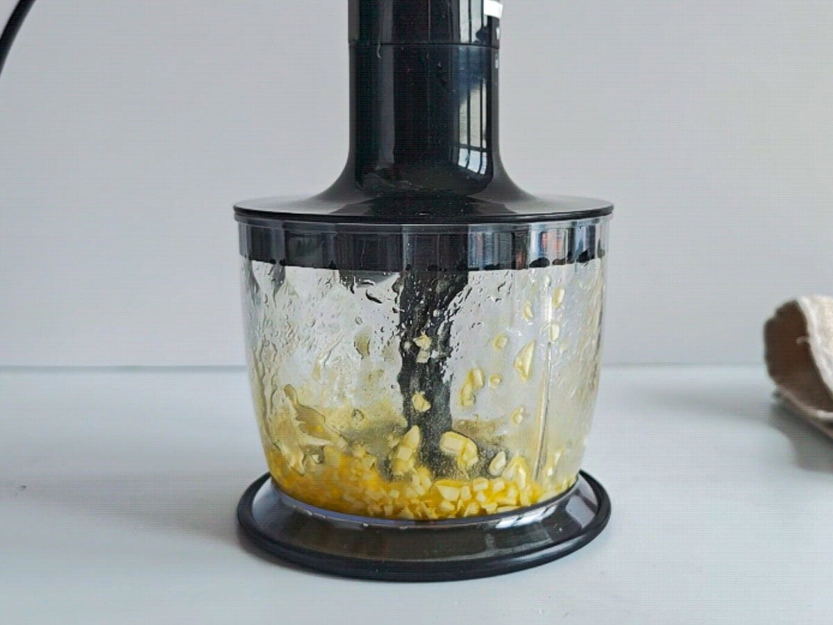 Low-calorie Basil Chimichurri (without excess oil) Garlic being blended with olive oil and lemon juice in a blender.