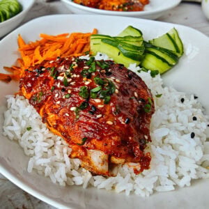 Easy Gochujang Chicken Thighs (Sticky & Oven-Baked) Gochujang chicken thigh served with rice and vegetables on a white plate.