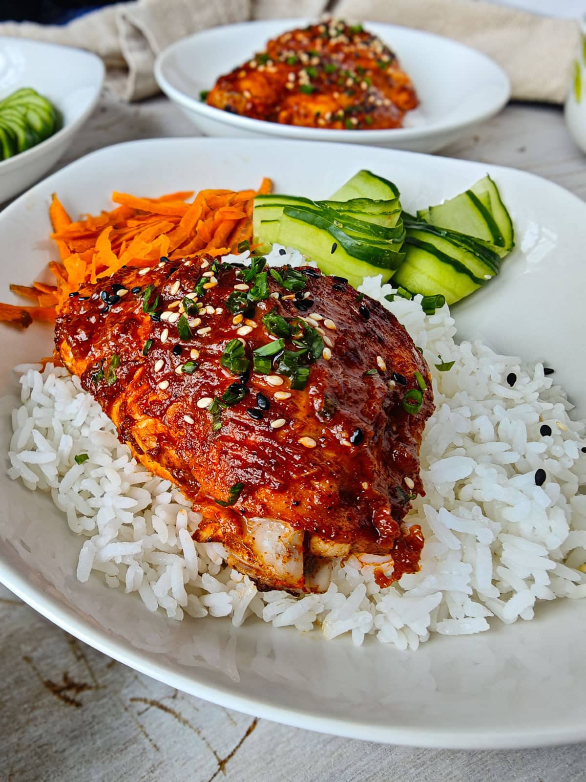 Gochujang marinated chicken served with rice and vegetables on a white plate, with a plate of gochujang chicken in the background.