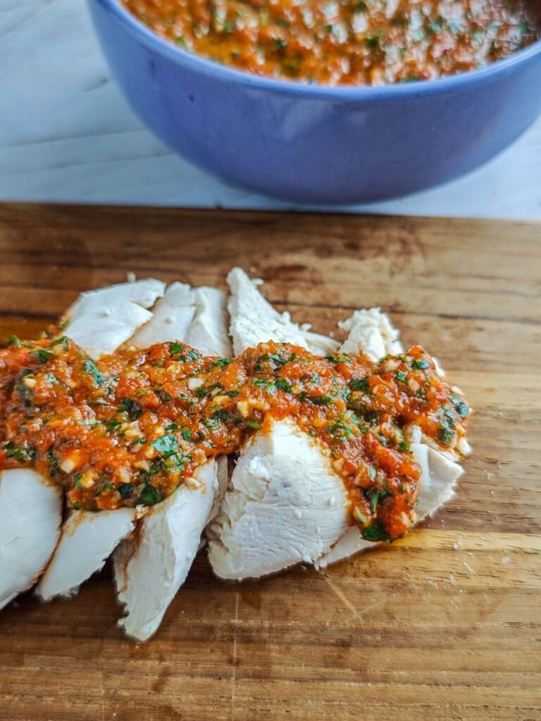 Red pepper chimichurri drizzled on poached chicken on a serving board.
