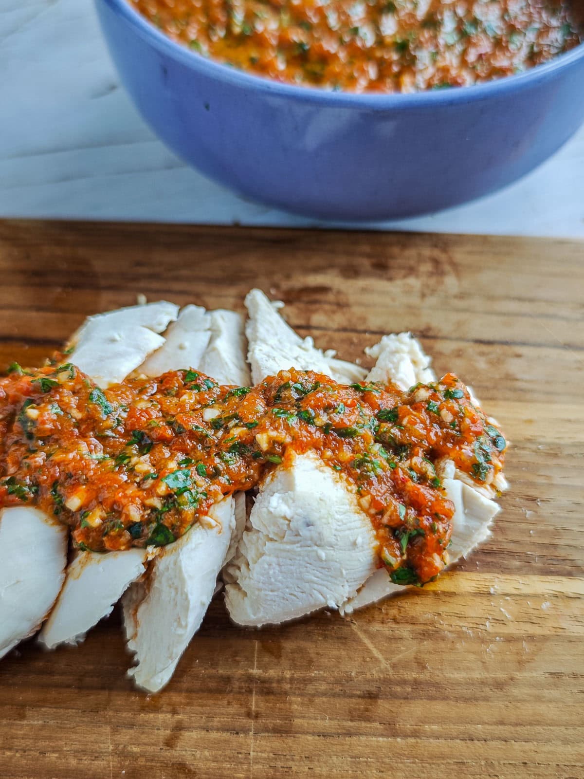 Easy Red Chimichurri Sauce with Roasted Peppers Red pepper chimichurri drizzled on poached chicken on a serving board.